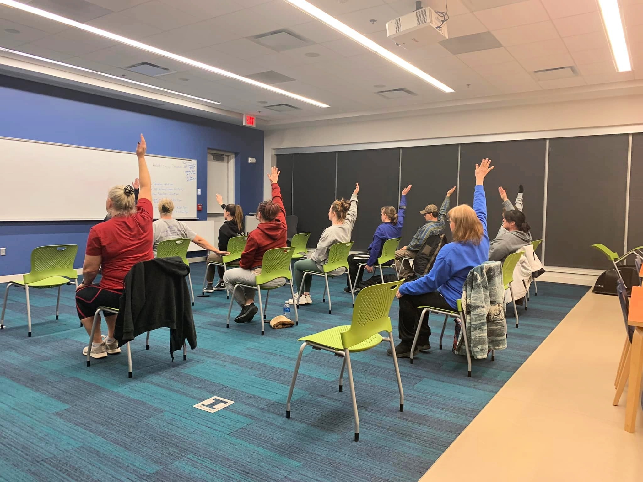 Adults sit in chairs and reach up during chair yoga