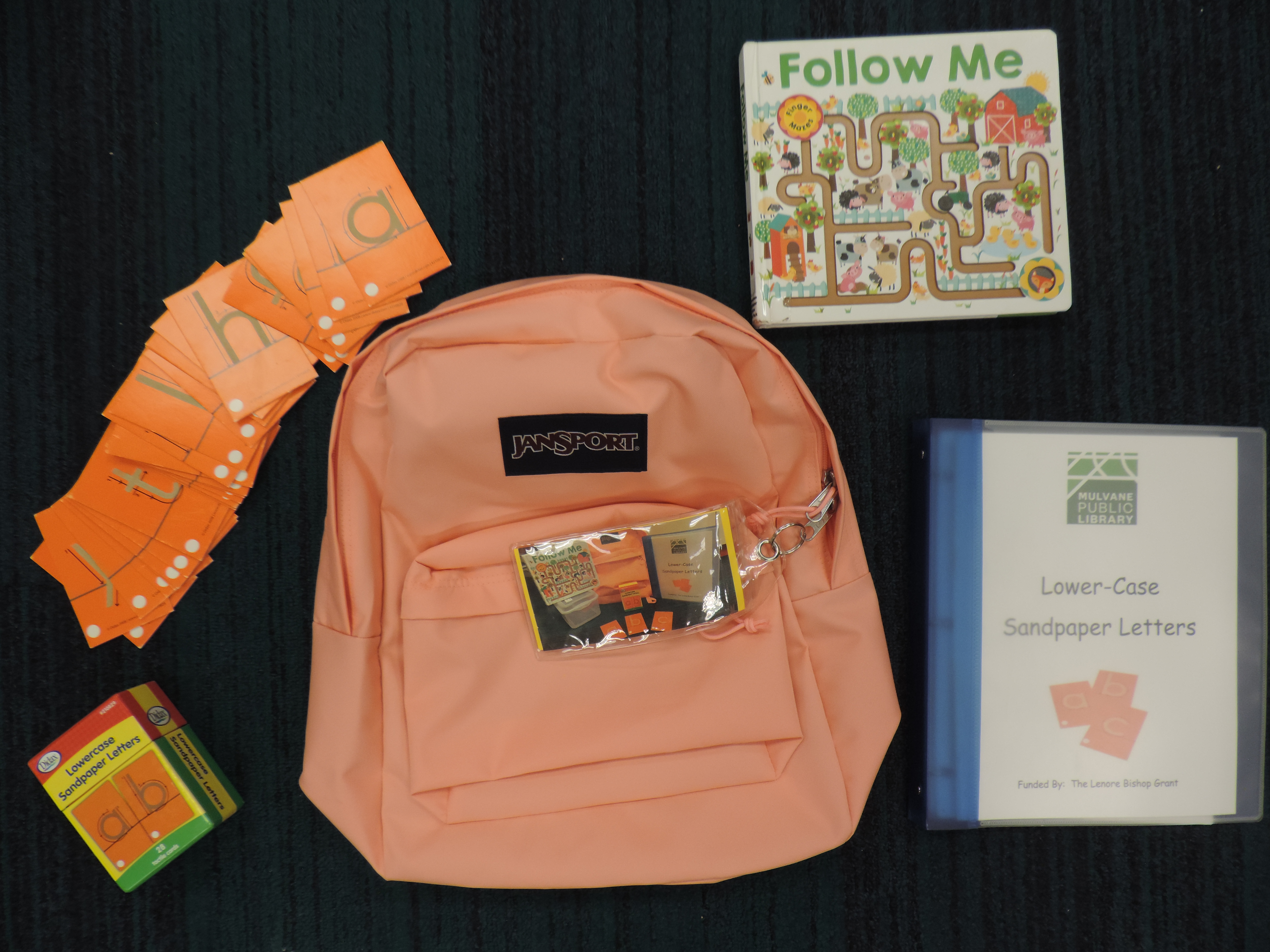 Orange backpack with book, plastic bin, and sandpaper letters