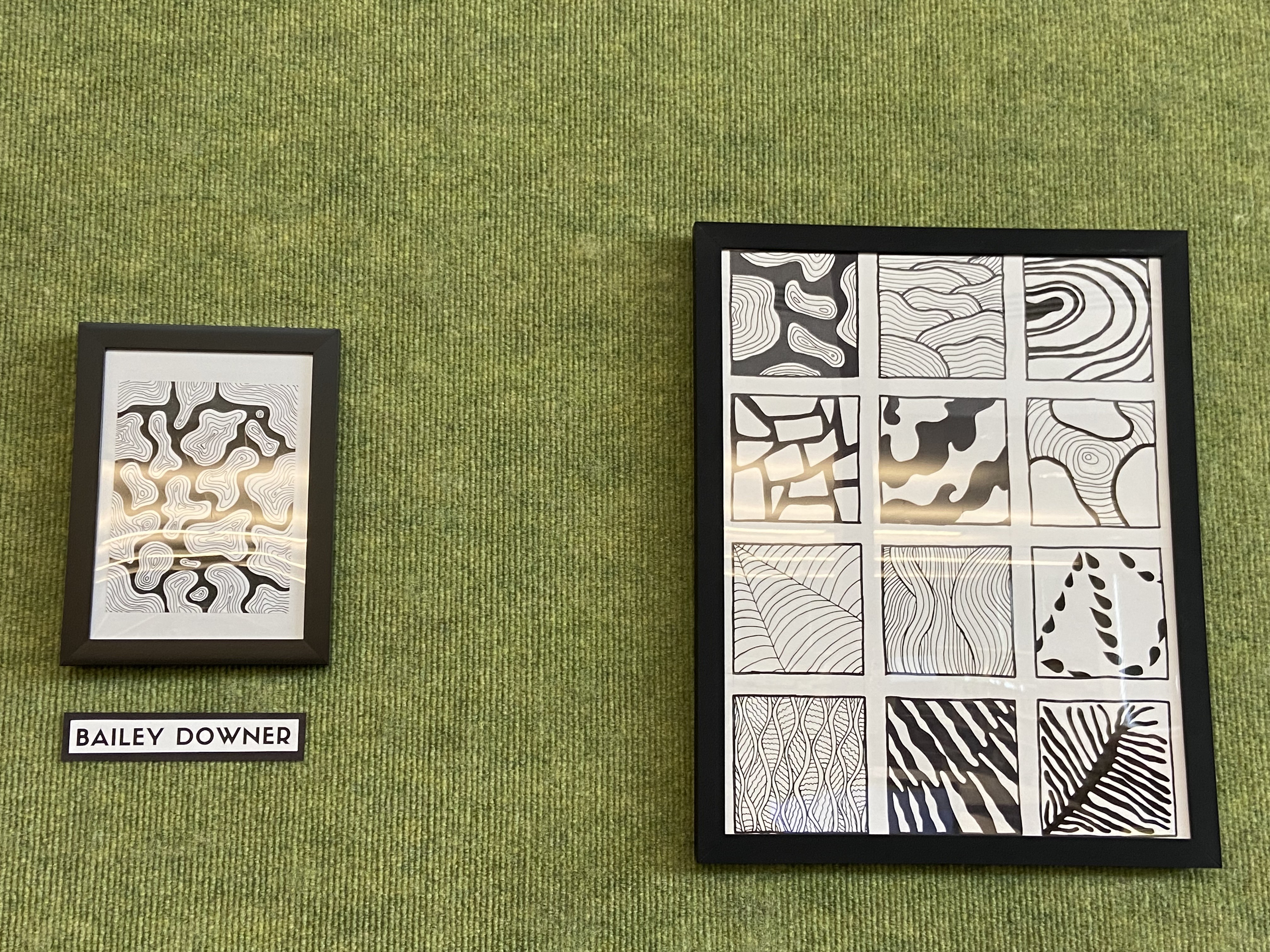 green wall with framed black and white drawings and name tag of artist
