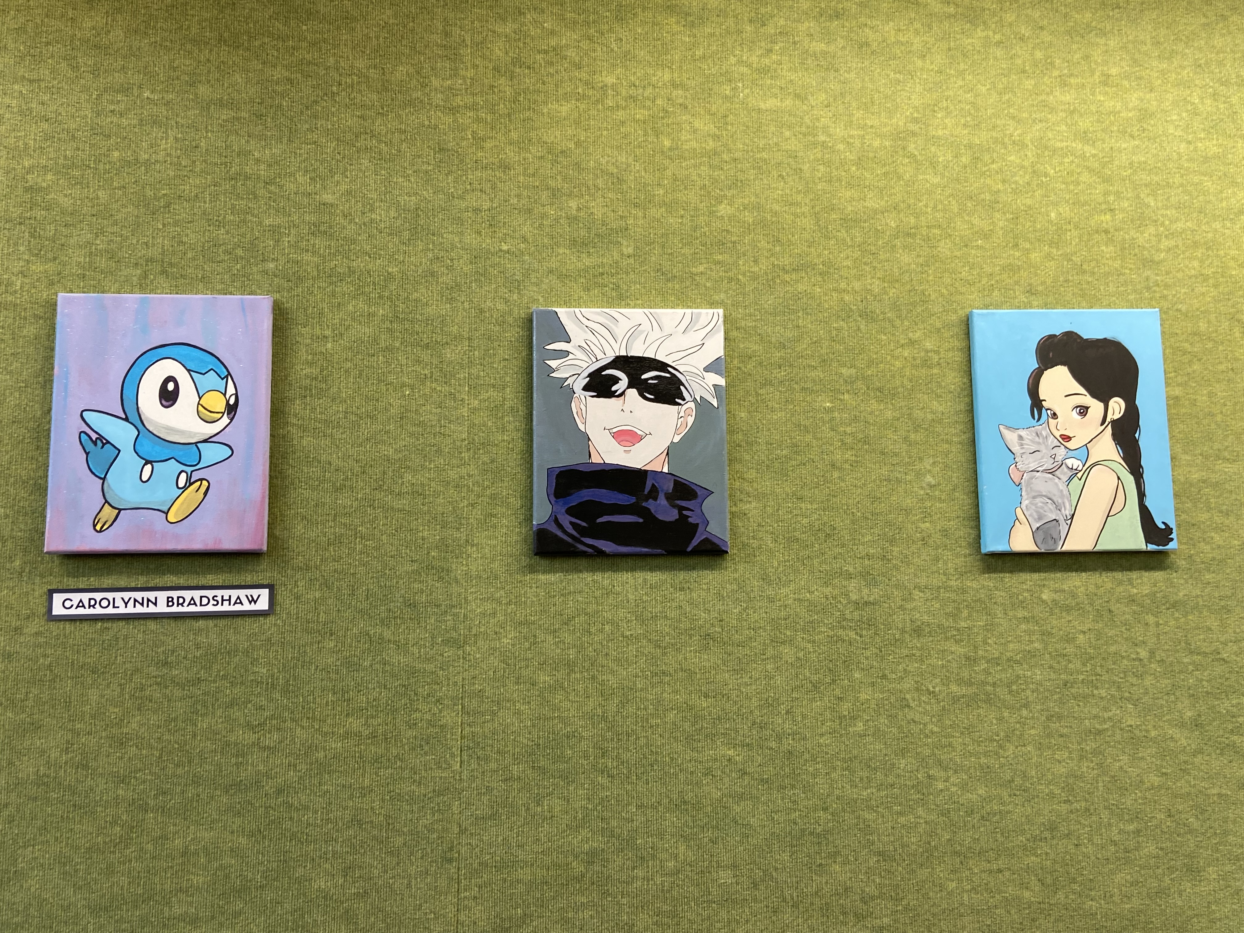 three anime art pieces on green textured wall