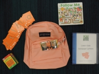 Orange backpack with book, plastic bin, and sandpaper letters